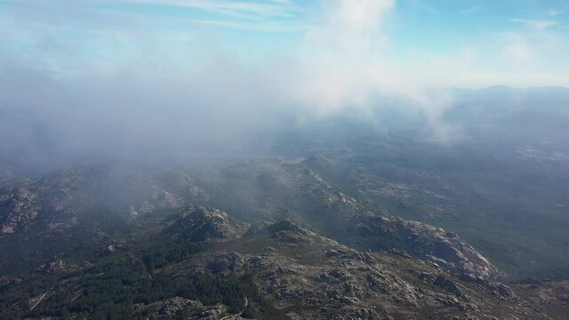 View from above, flying above the clouds, stunning aerial view of a granitic massif surrounded by moving clouds during a sunny day. Mount Limbara (Monte Limbara) Sardinia, Italy.
