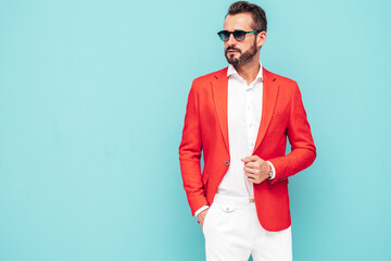 Portrait of handsome confident stylish hipster lambersexual model.Sexy modern man dressed in elegant red suit. Fashion male posing in studio near blue wall in sunglasses