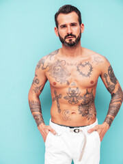 Fototapeta premium Portrait of handsome confident stylish hipster lambersexual model. Sexy modern man. Naked torso with tattoos.Fashion male posing in studio near light blue wall