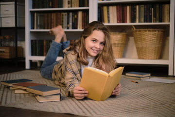 girl sits on the couch and reads a book, a tablet and headphones lie next to it. modern teenager at home. teen literature concept.