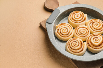Baking dish with uncooked cinnamon rolls on color background