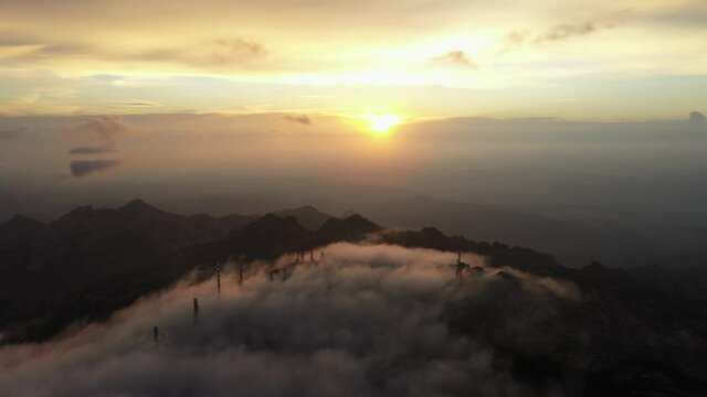 View from above, flying above the clouds, stunning aerial view of a mountain range with an antenna farm surrounded by clouds during a beautiful sunrise. Mount Limbara (Monte Limbara) Sardinia, Italy.