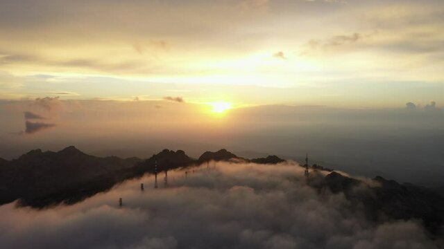 View from above, flying above the clouds, stunning aerial view of a mountain range with an antenna farm surrounded by clouds during a beautiful sunrise. Mount Limbara (Monte Limbara) Sardinia, Italy.