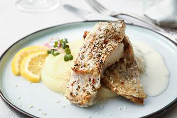 Plate with baked cod fillet, sauce and mashed potatoes on table in restaurant