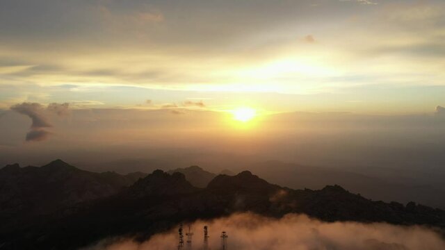View from above, flying above the clouds, stunning aerial view of a mountain range with an antenna farm surrounded by clouds during a beautiful sunrise. Mount Limbara (Monte Limbara) Sardinia, Italy.