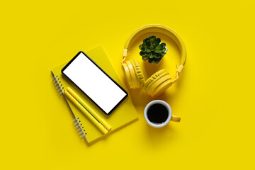 Modern mobile phone, headphones, houseplant and cup of coffee on yellow background