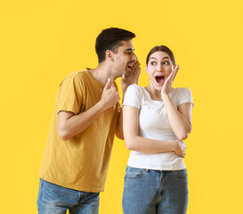 Young man sharing gossip with his wife on yellow background