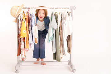 Shopping, kleines Mädchen schaut durch einen Kleiderständer fröhlich. Weißer Hintergrund Vs1