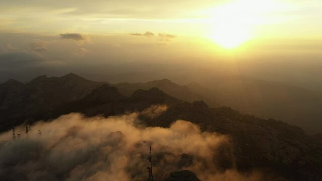 View from above, flying above the clouds, stunning aerial view of a mountain range with an antenna farm surrounded by clouds during a beautiful sunrise. Mount Limbara (Monte Limbara) Sardinia, Italy.