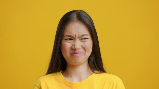 Disgusted Chinese Lady Smelling Unpleasant Stinky Smell Over Yellow Background