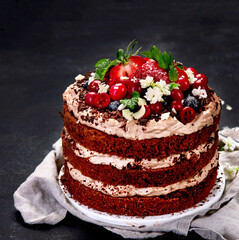 Delicious homemade chocolate cake with fresh berries and mascarpone cream on dark background.