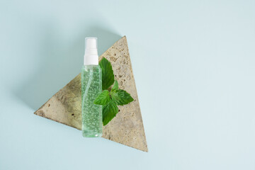 cosmetic bottle with green gel and fresh mint on triangular stone blue background. skin care product with peppermint oil
