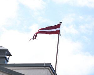 Overcast sky view of red and white colored Latvia national country flag floating n the mast.
