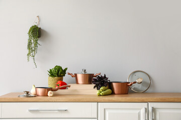 Set of copper cooking pots with vegetables on counter near light wall