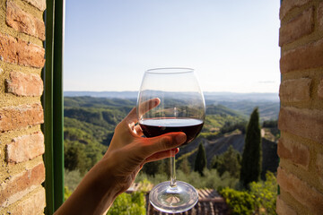 Woman holding a glass of red wine with beautiful landscape of Italy in a background on a sunny day....