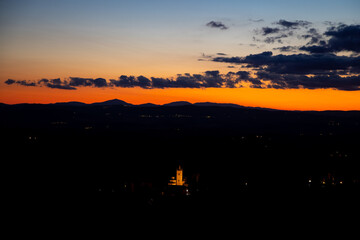 Beautiful dramatic sunset in Italy. Colorful sky with some clouds, black earth at dusk and monastery Abbazia di Monte Oliveto. End of the day