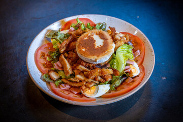 Salad with ham, cheese and chicken on a black background, on a white plate