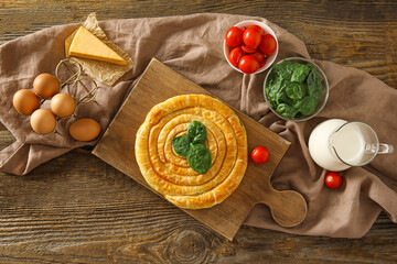 Board with tasty spinach pie and ingredients on wooden background