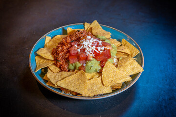 Nachos with guacamole and tomato sauce on a black background, on a blue plate