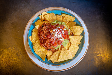 Nachos with guacamole and tomato sauce on a black background, on a blue plate