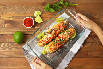 Woman with baking dish of tasty Elote Mexican Street Corn on wooden background