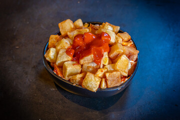Patatas bravas with tomato ketchup sauce on a black background, on a blue plate