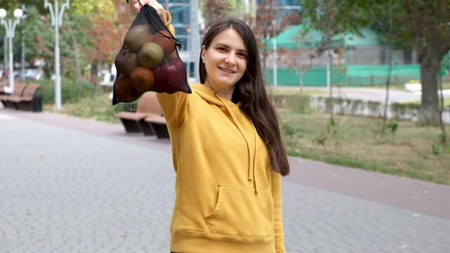 A brunette woman shows a fruit mesh fabric bag with vegetables and fruits.