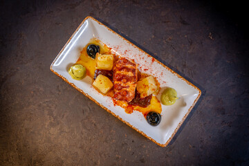 Octopus tentacle with potatoes on a black background, on a white plate