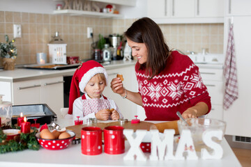 Cute blond child, boy and his mom, baking christmas cookies at home