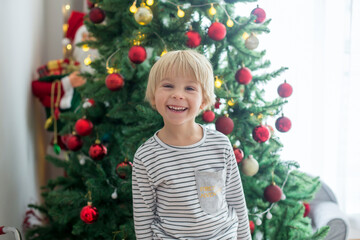 Beautiful toddler child, decorating   Christmas tree, presents under the trees
