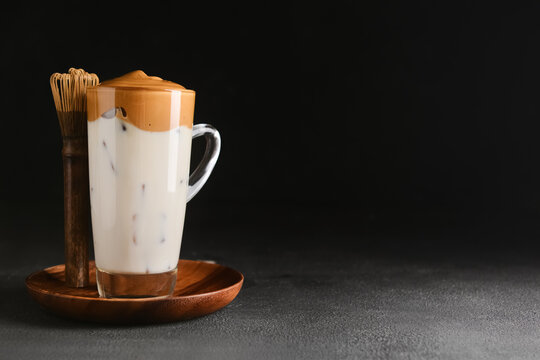 Glass cup of tasty dalgona hojicha latte and chasen on dark background