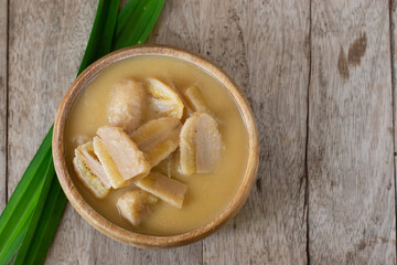 Banana in coconut milk, Thai dessert in wooden bowl with pandan leaf on wooden background.
