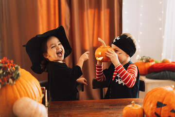 Boy in pirate costume holding pumpkin and girl in witch costume laughing.