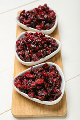 Bowls with tasty dried cranberries on light wooden background, closeup