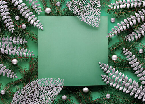 Green Silver Christmas Background With Square Copy-space, Place For Text. Natural Xmas Twigs Decorated With Silver Exotic Deco Leaves And Glass Baubles, Balls. Flat Lay. Top View On Dark Green Paper.