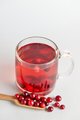 Cup of tasty cranberry tea and scoop with berries on white background