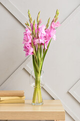 Vase with beautiful gladiolus flowers and books on table in room