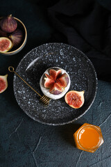 Obraz na płótnie Canvas Plate with cheese, ripe figs and jar of honey on dark background