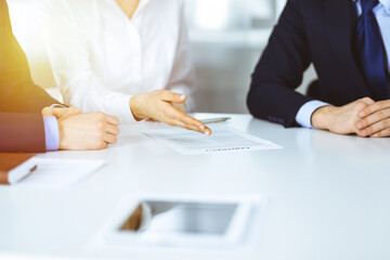 Group of business people, men and a woman, discuss details of a contract at meeting in a sunny modern office. Discussion at negotiation or workplace. Teamwork, partnership and business concept