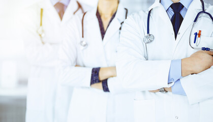Group of modern doctors standing as a team with crossed arms and stethoscopes in a sunny hospital office. Physicians ready to examine and help patients. Medical help, insurance in health care, best