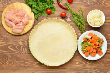 Baking dish with fresh dough and ingredients for chicken pot pie on wooden background