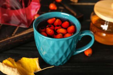 Cup of tasty rose hip tea on black wooden background