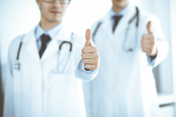 Two male doctors standing as a team and showing thumbs up as a symbol of the best service for patients in the clinic. Medicine and health care