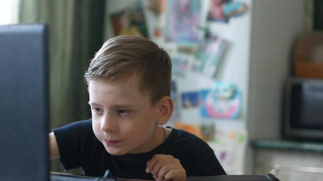 Caucasian schoolboy 7-9 years old performs homework while sitting at a laptop at home. The correct answer when solving a school problem. Have an idea of the emotion of a child. Finger gesture idea