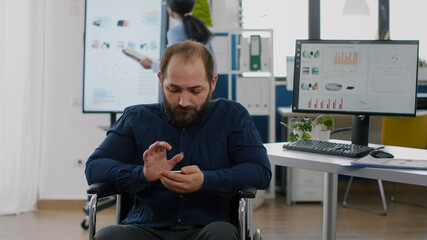 Immobilized invalid paralyzed handicapped young employee searching on mobile phone during worktime...