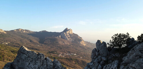 A steep cliff. A steep rocky mountain against the background of a valley and a clear sky. A mountain peak with growing trees.