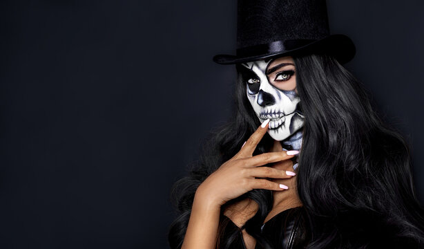 Beautiful model in Halloween makeup on black background. Sexy woman in top hat and skull makeup. Halloween makeup concept.