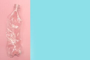 Used and crumpled plastic bottle on pink and blue background with a place for text. Recycling concept. Rumpled. Reasonable consumption. Flat lay. Copy space.