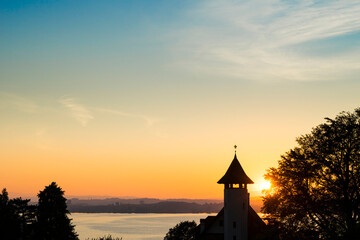 Fototapeta premium Sunset over Lake Zugersee from the Swiss town of Zug, silhouetted by a church tower.