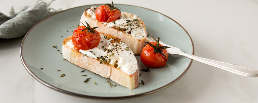 a plate of bruschetta with cream cheese and baked tomatoes on a light marble table